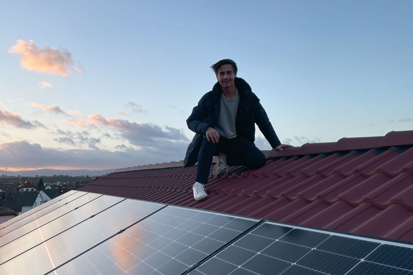Samuel Kutger auf einem Ziegeldach neben einer Solaranlage bei Sonnenuntergang